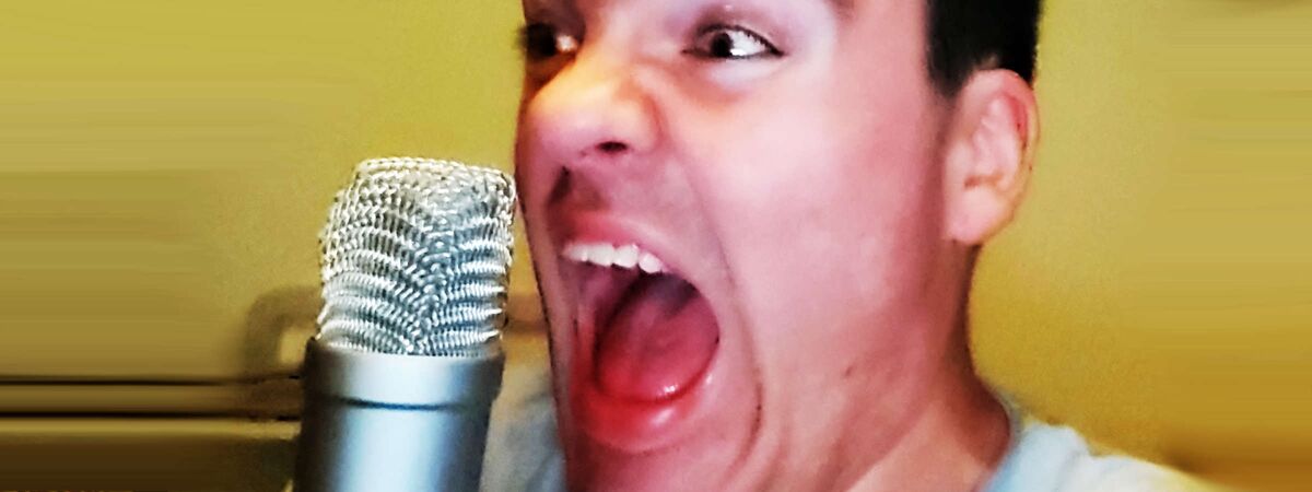 Stimmenwandler Christopher Zunke schreit emotional aufgeladen ins Mikro. Sein Mund ist weit geöffnet, Augen blicken erschrocken in die Ferne. Foto einer Tonaufnahme für ein schauriges Hörspiel. Sprecher spielt einen psychotisch-wahnsinnigen Charakter.